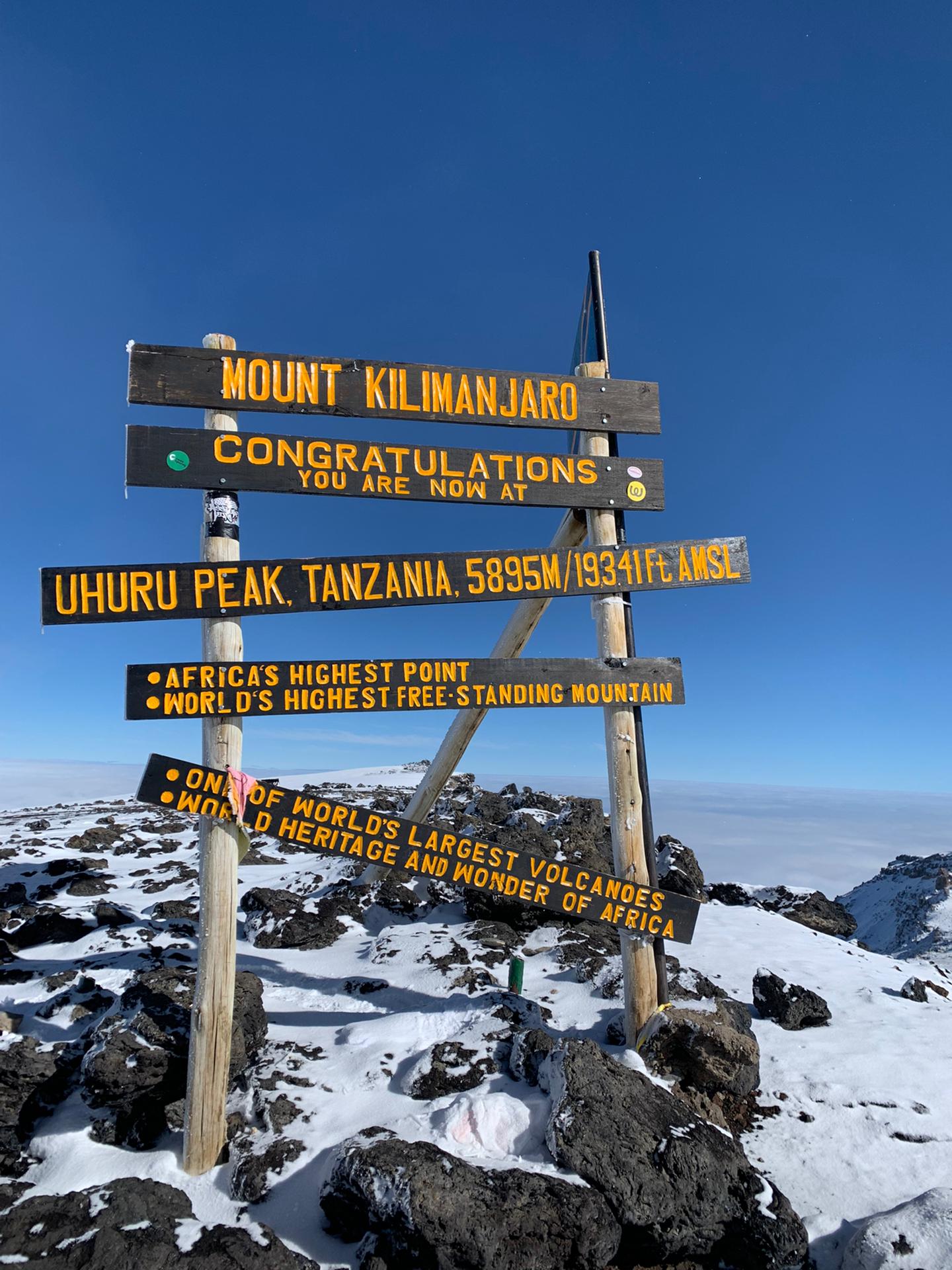 Das hölzerne Gipfelschild am Uhuru Peak auf 5.895 Metern, umgeben von Schnee und dunklem Lavagestein
